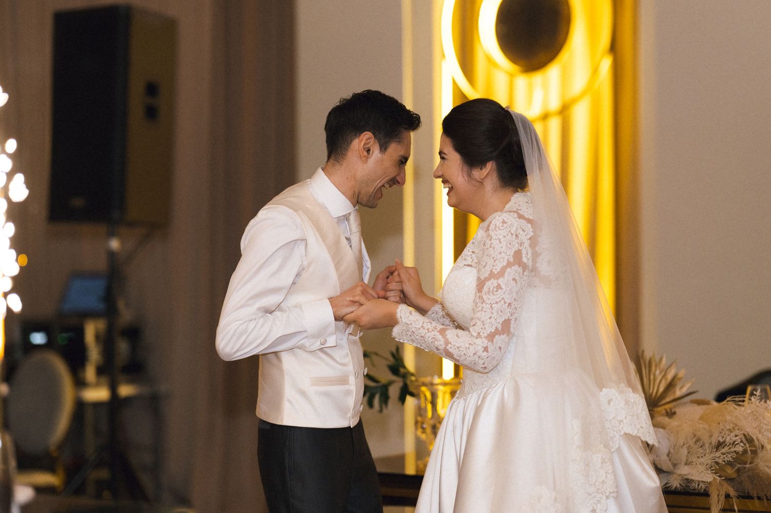 Bride and groom share a tender moment during their wedding reception, holding hands and smiling at each other.