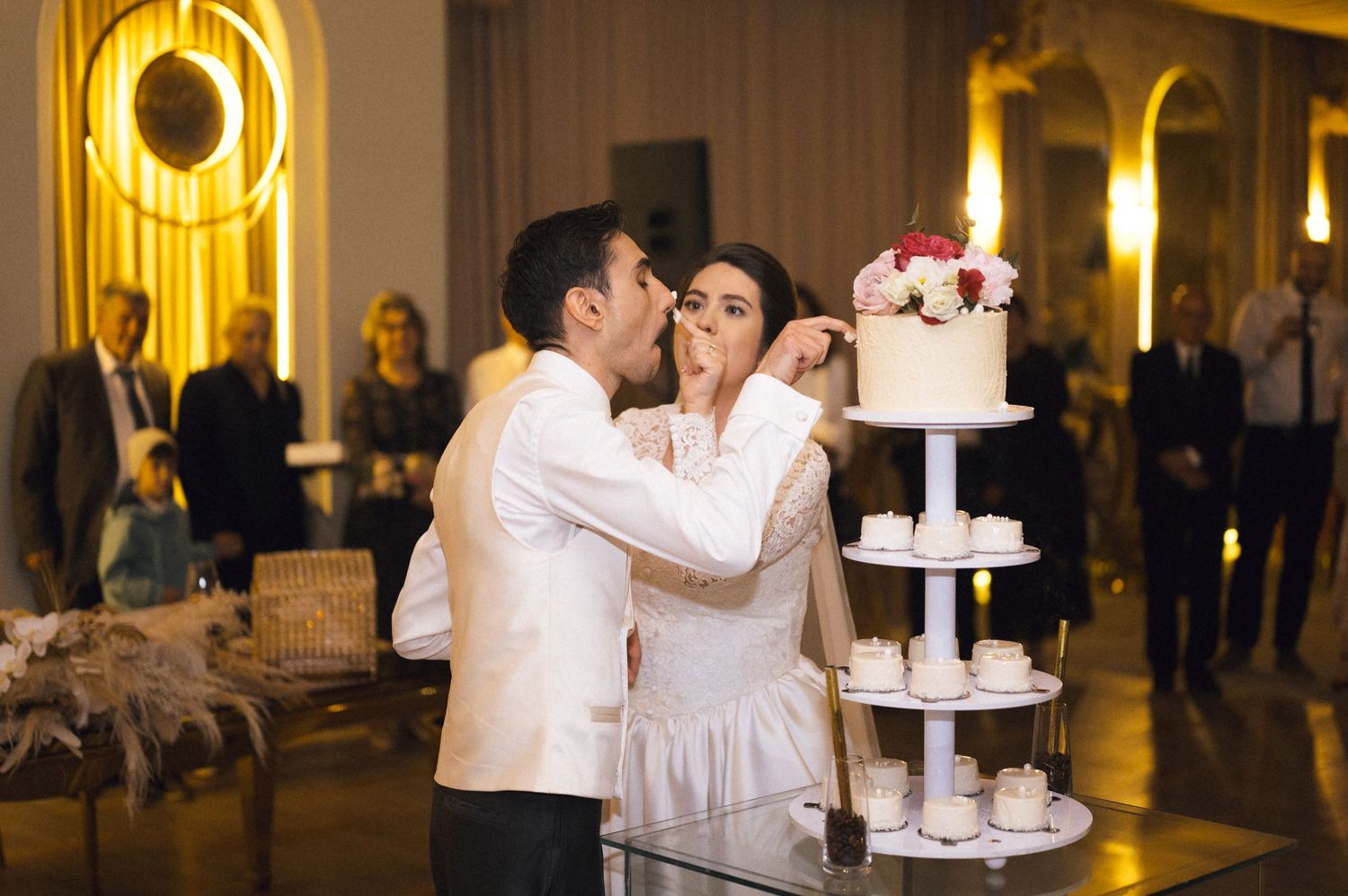 Bride and groom sharing wedding cake at elegant reception with tiered white cake display.