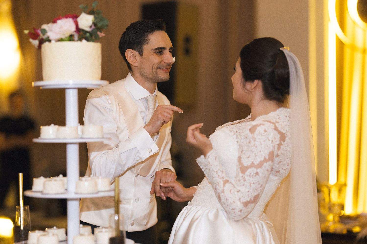 Bride and groom sharing a joyful moment cutting their elegant white wedding cake at a formal reception.