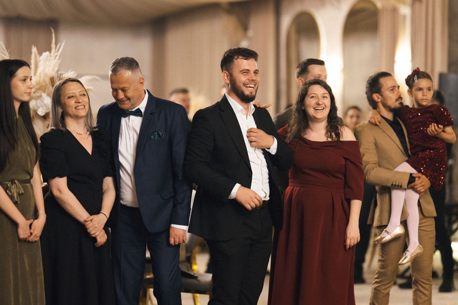 Elegantly dressed guests smiling and socializing at a formal event in a decorated banquet hall.