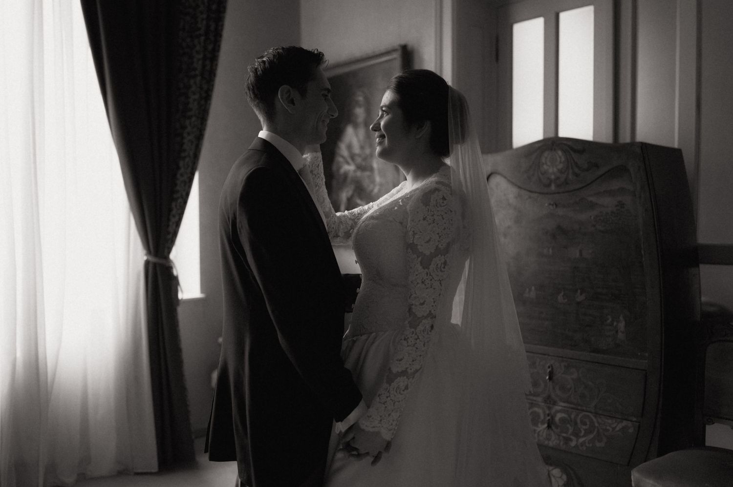 Black and white photo of a bride and groom sharing a tender moment in an elegant room on their wedding day.