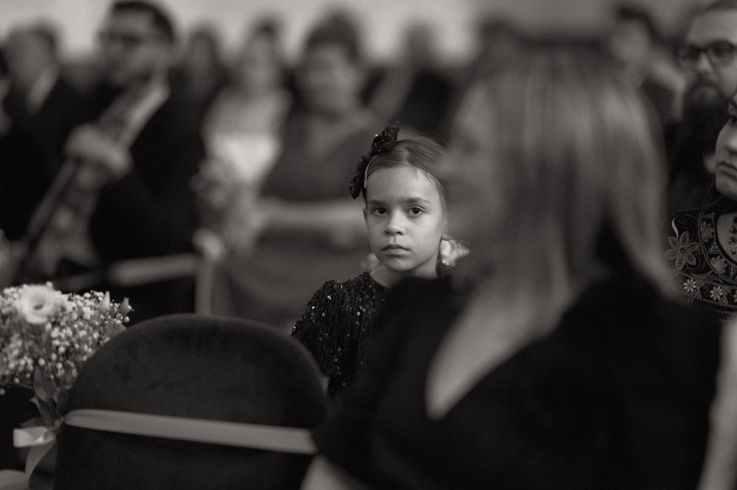 Black and white photo of a young girl sitting in church pews, gazing forward during a ceremony.