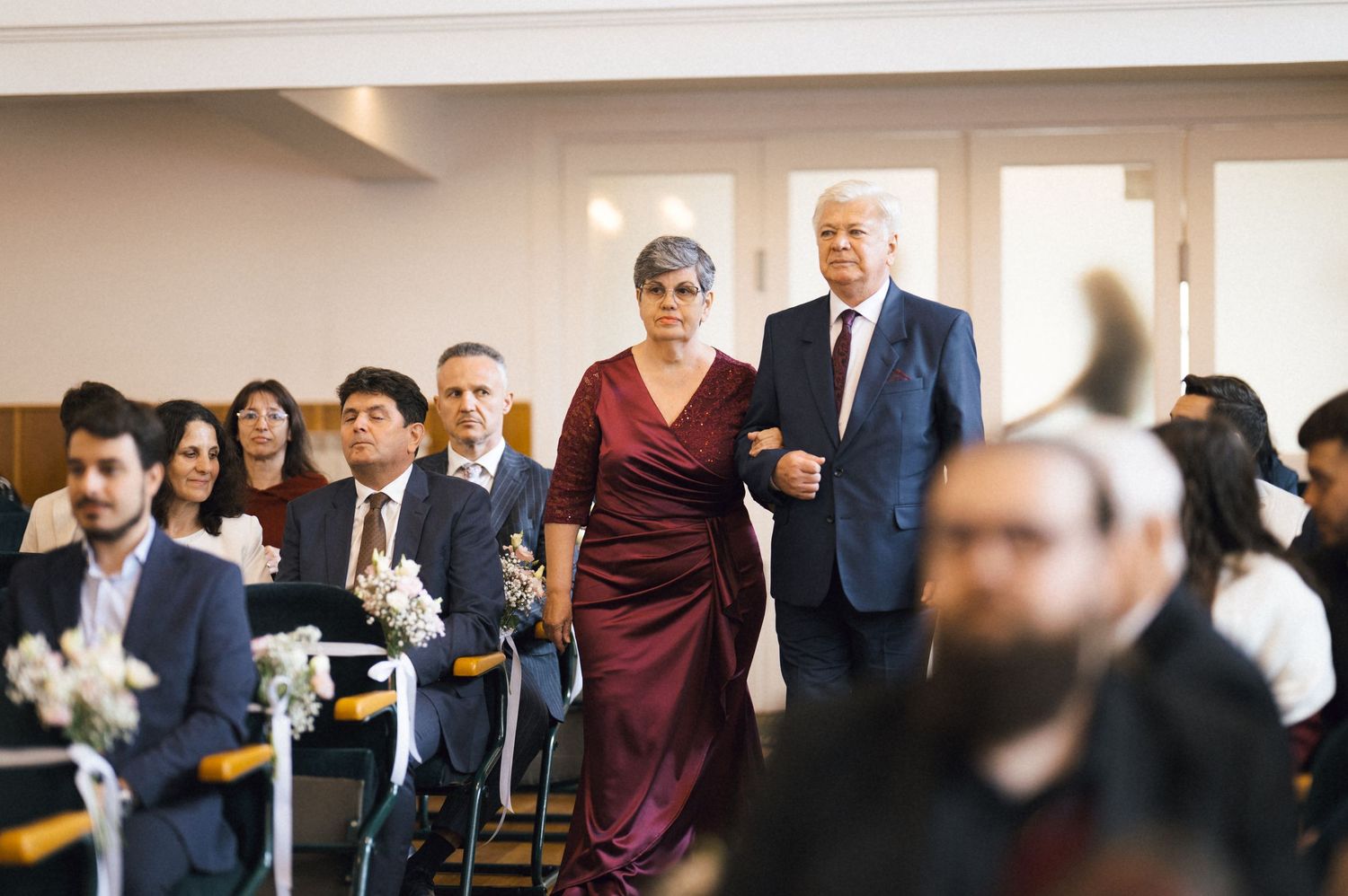 Elegant wedding ceremony guests seated in rows as a couple walks down the aisle in a formal indoor venue.