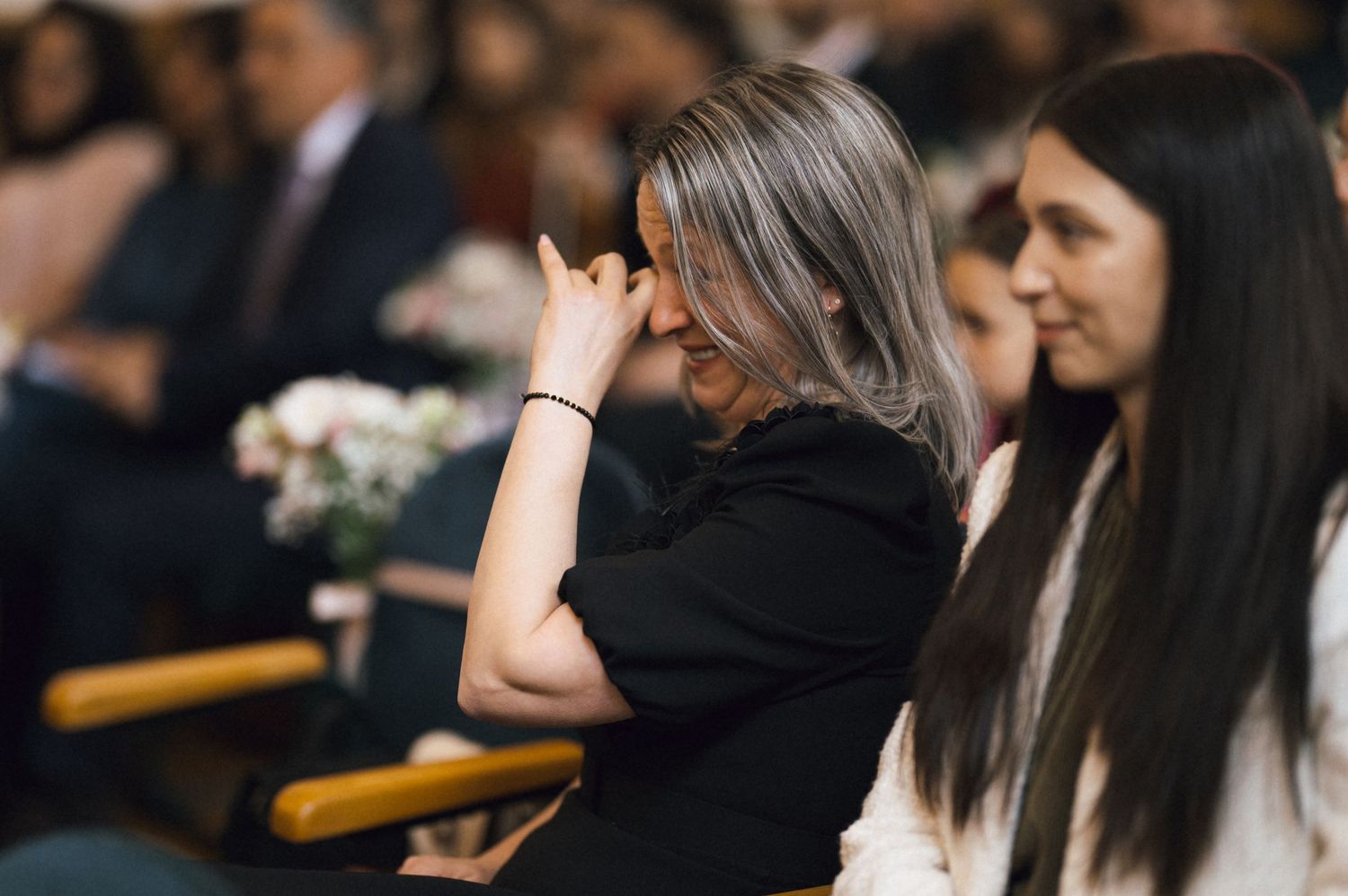 Woman in black bowing head in prayer during a church service, seated in wooden pews with others nearby.