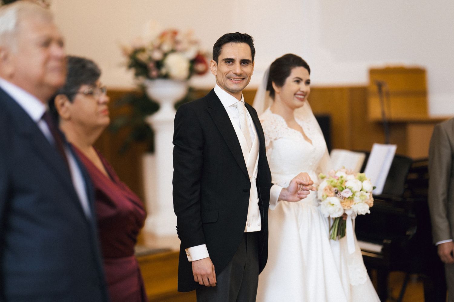 Bride and groom smiling during wedding ceremony in church, bride holding white floral bouquet.