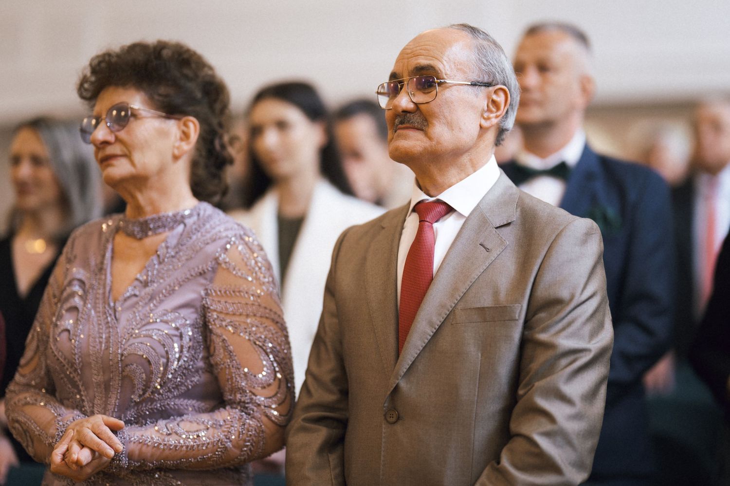Elegant older couple dressed formally standing together at a wedding ceremony in a grand venue.
