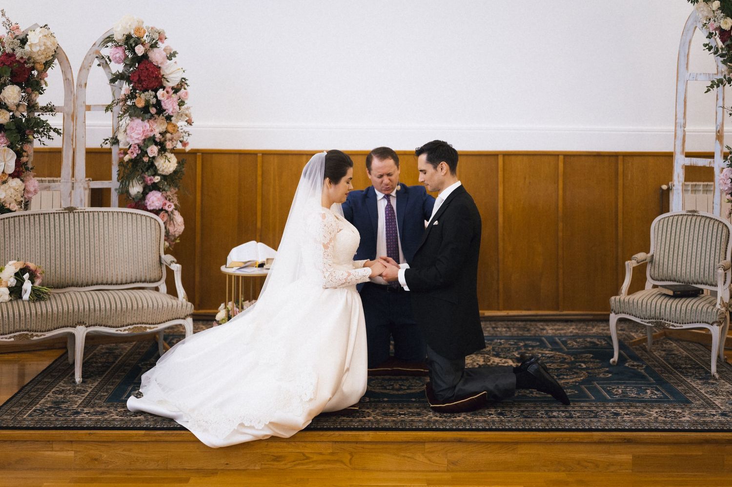 Bride and groom exchange vows at elegant indoor wedding ceremony with floral arrangements and officiant.
