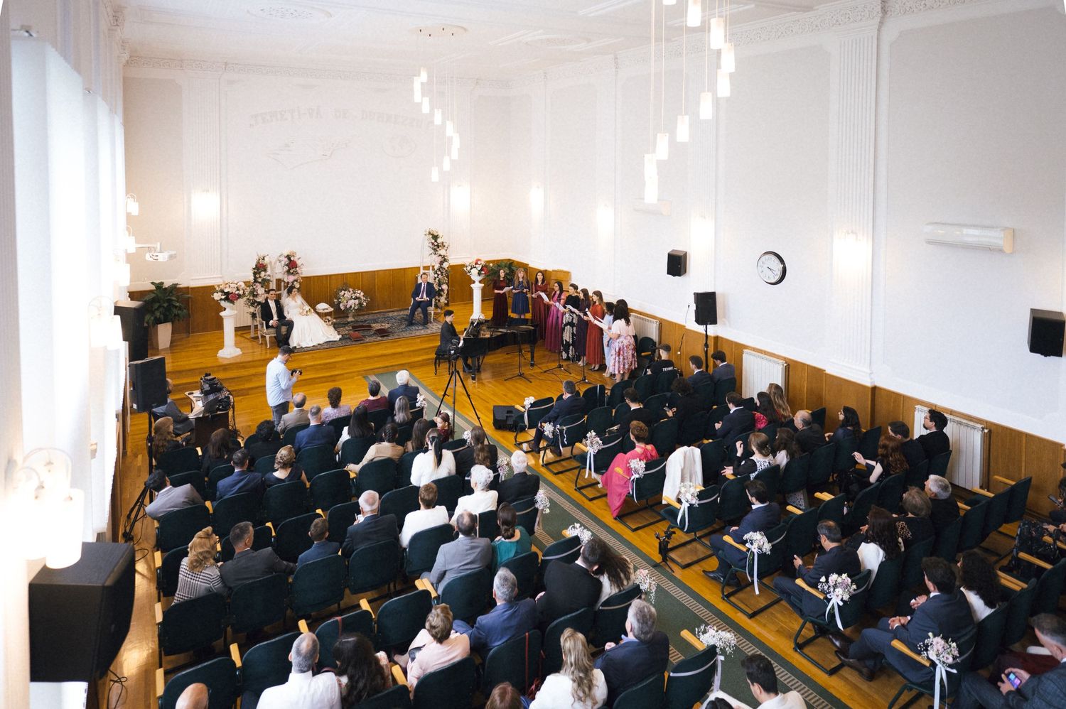 Elegant wedding ceremony in a grand white hall with seated guests watching the couple at the altar.