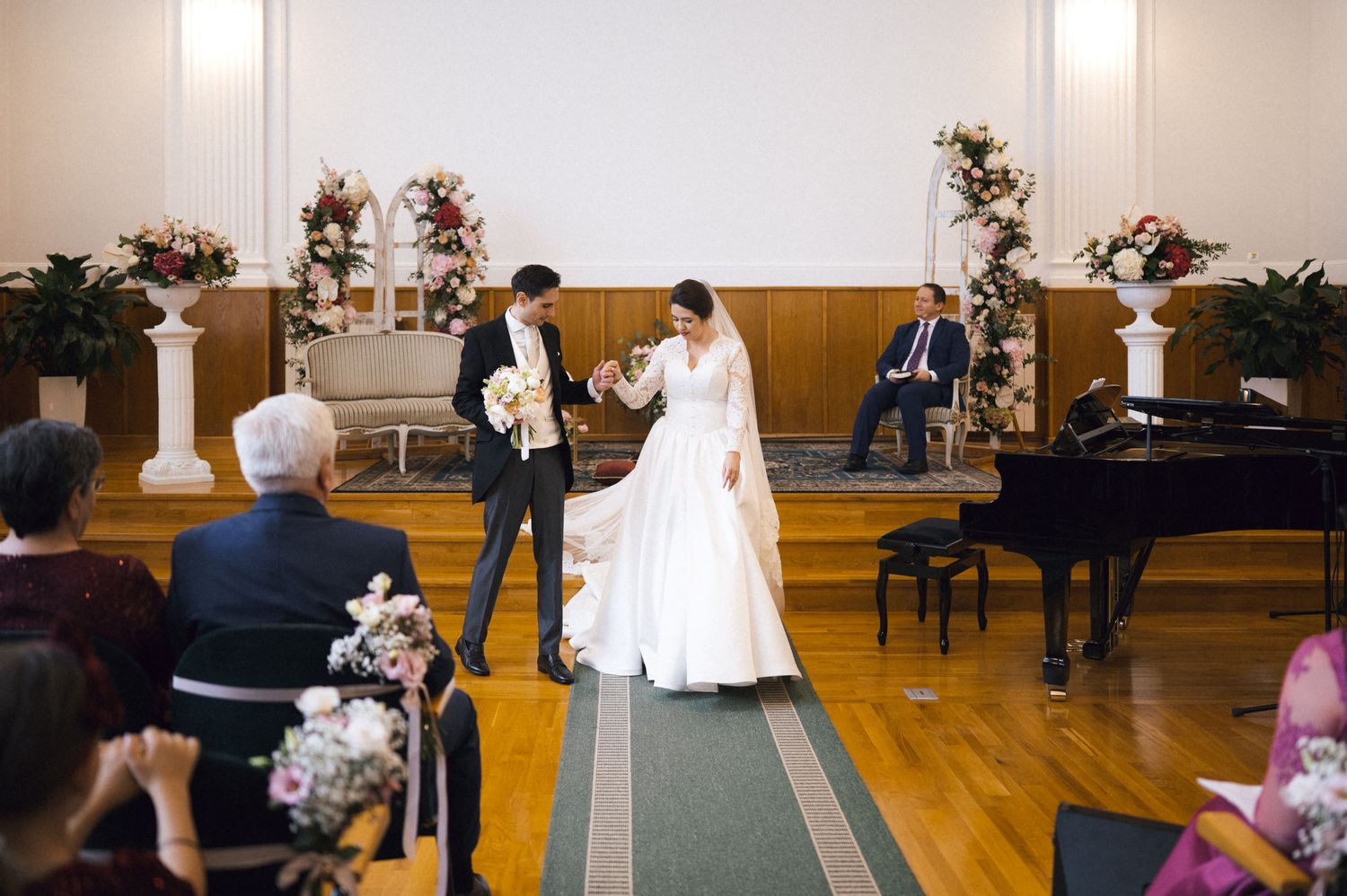 Bride and groom walk down the aisle in an elegant chapel wedding ceremony with floral arrangements and a grand piano.