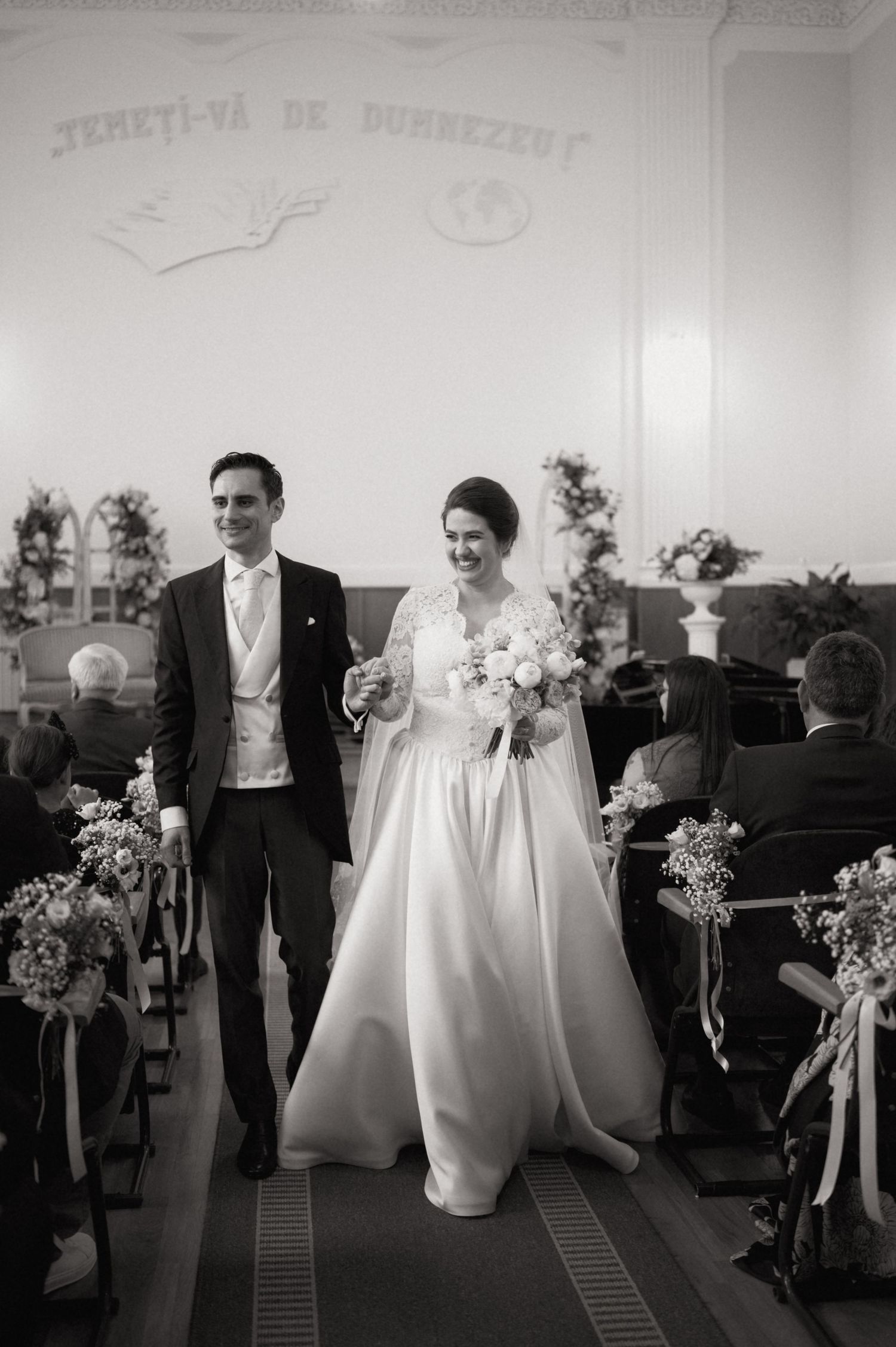 Black and white photo of a smiling bride and groom walking down the aisle after their wedding ceremony.