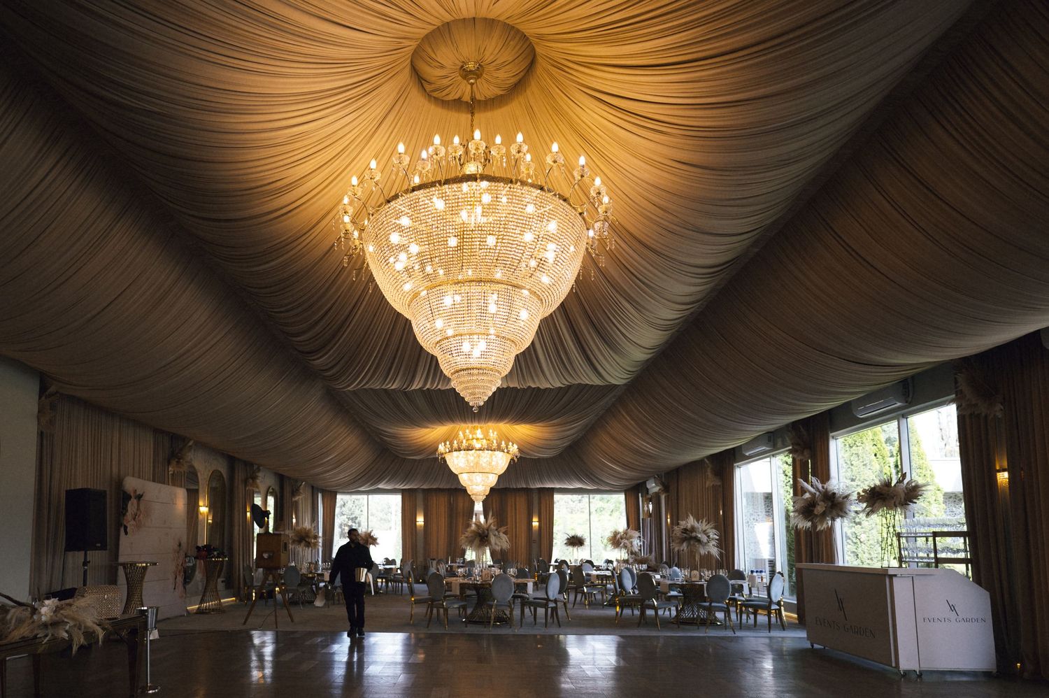 Elegant banquet hall with crystal chandeliers, draped ceiling, and long dining tables set for a formal event.