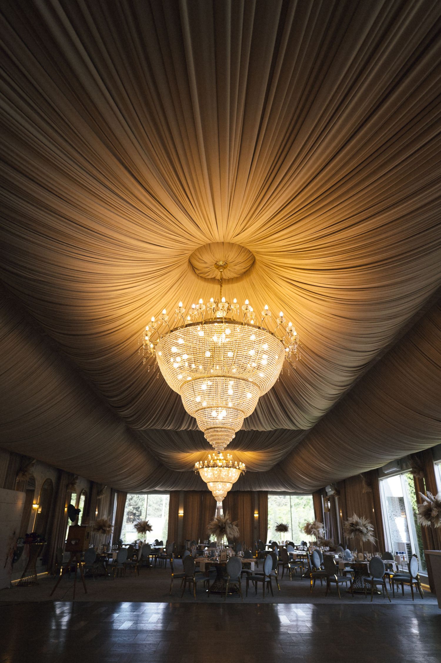 Elegant banquet hall with cascading crystal chandeliers and draped fabric ceiling, set for a formal event with round tables.