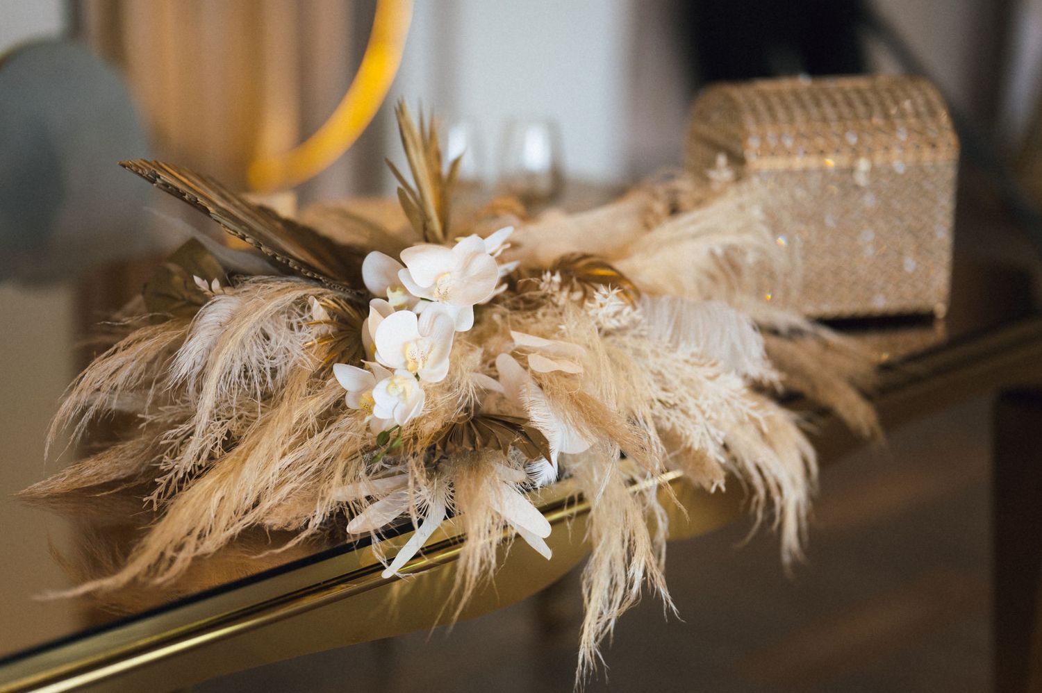 Elegant feather and dried floral arrangement with white blooms on a gold surface, perfect for wedding decor.