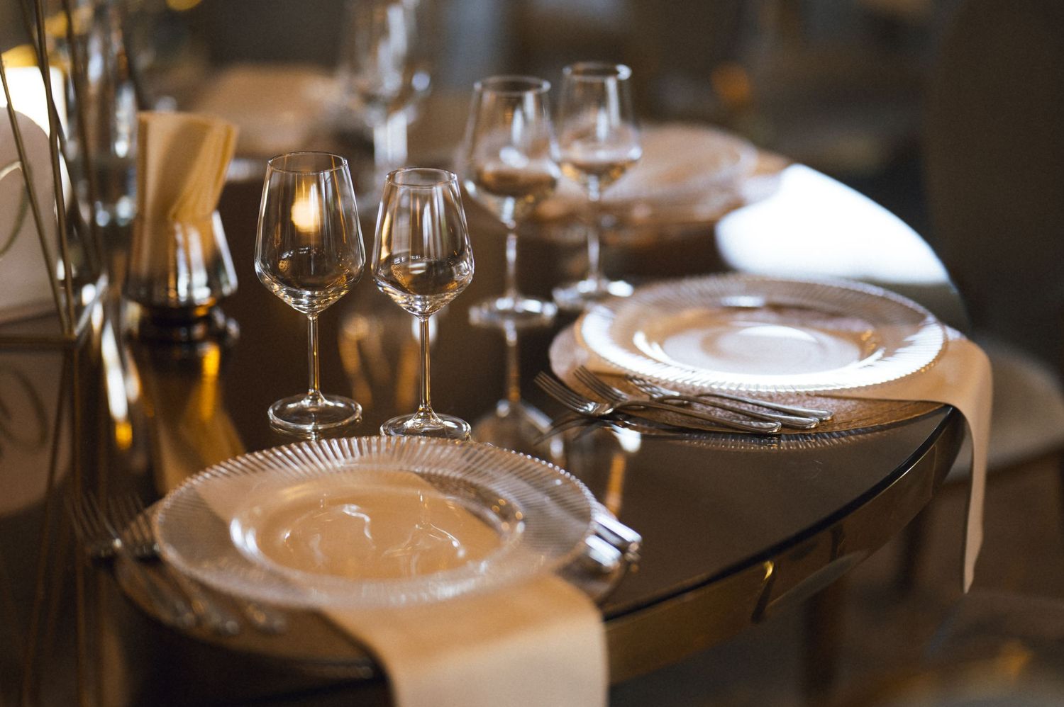 Elegant fine dining table setting with crystal wine glasses, silver charger plates, and golden napkins.