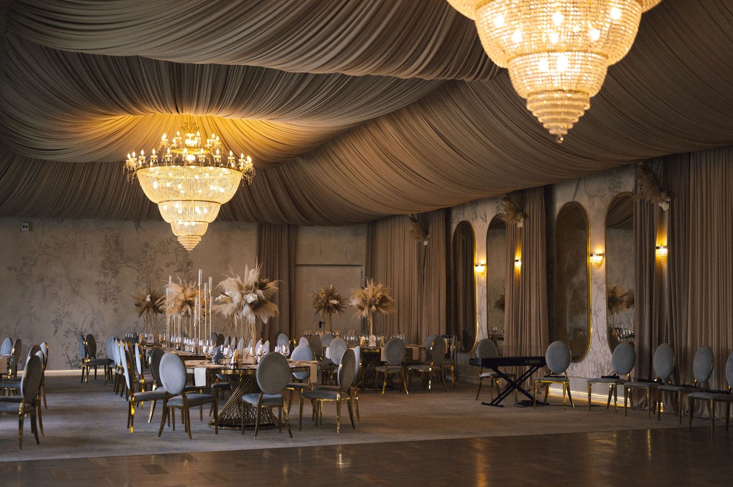 Grand ballroom with draped ceiling, crystal chandeliers, marble columns, and elegant table settings for a luxury wedding reception.