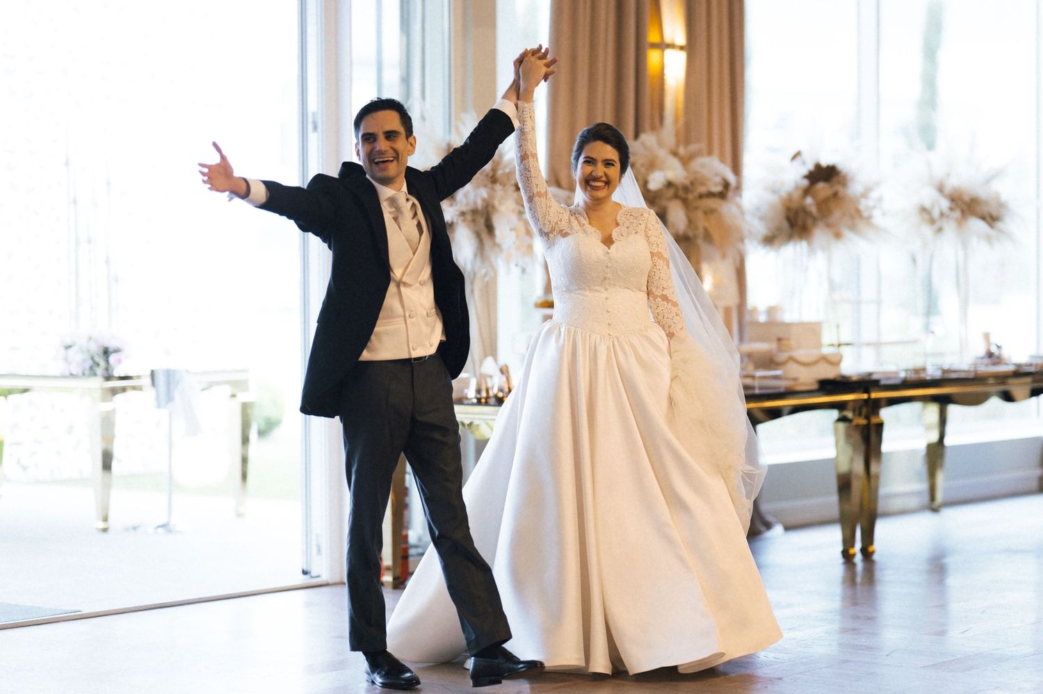 Joyful newlyweds celebrate their wedding reception entrance, bride in white gown, groom in black tuxedo, elegant venue.
