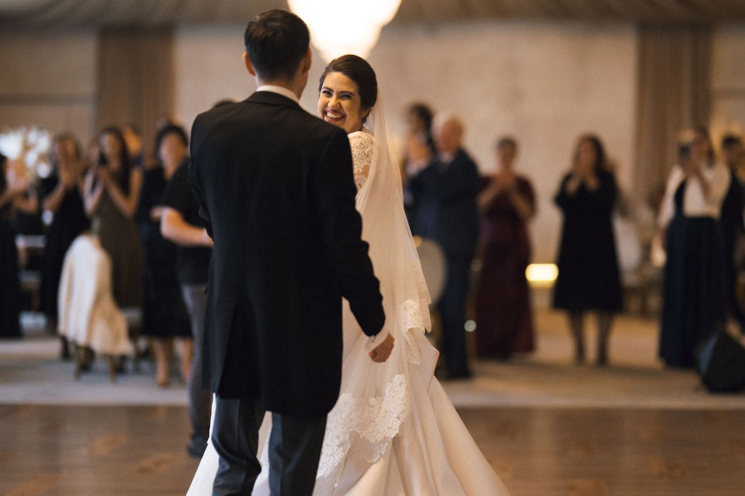 Bride and groom share their first dance at a wedding reception, surrounded by guests in formal attire.