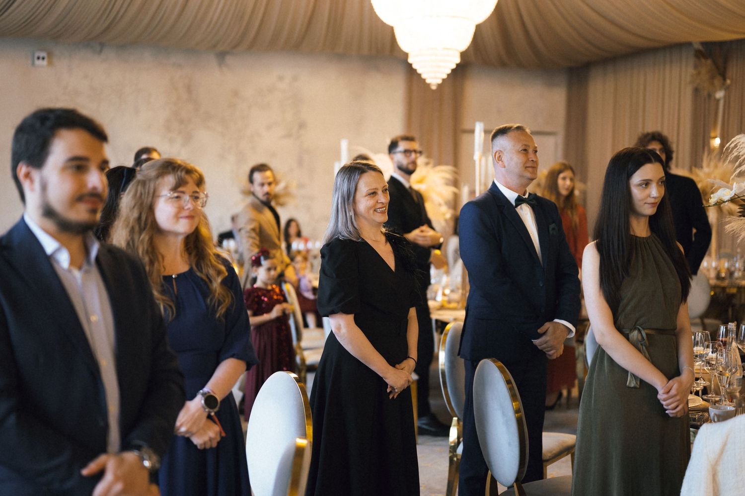 Elegantly dressed guests standing at a formal wedding reception in a beautifully decorated ballroom venue.