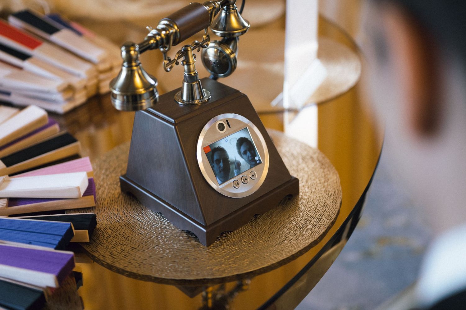 Vintage antique telephone with brass accents on a gold glass table next to colorful books in an elegant setting.