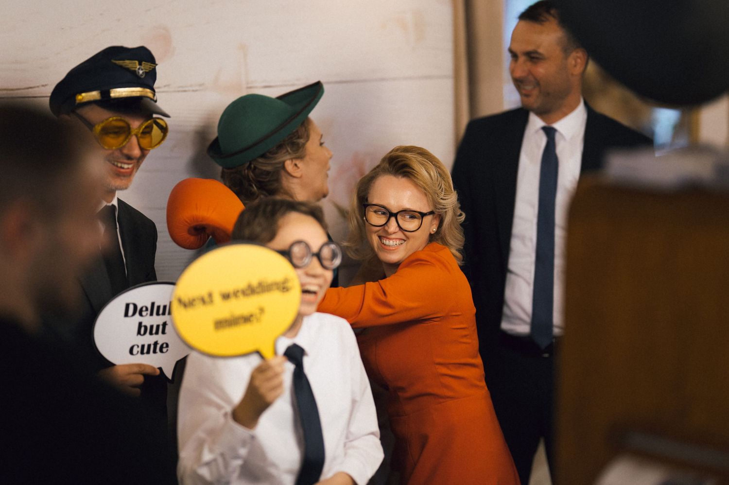 Group of friends in fun costumes hugging and laughing at a wedding photo booth celebration.