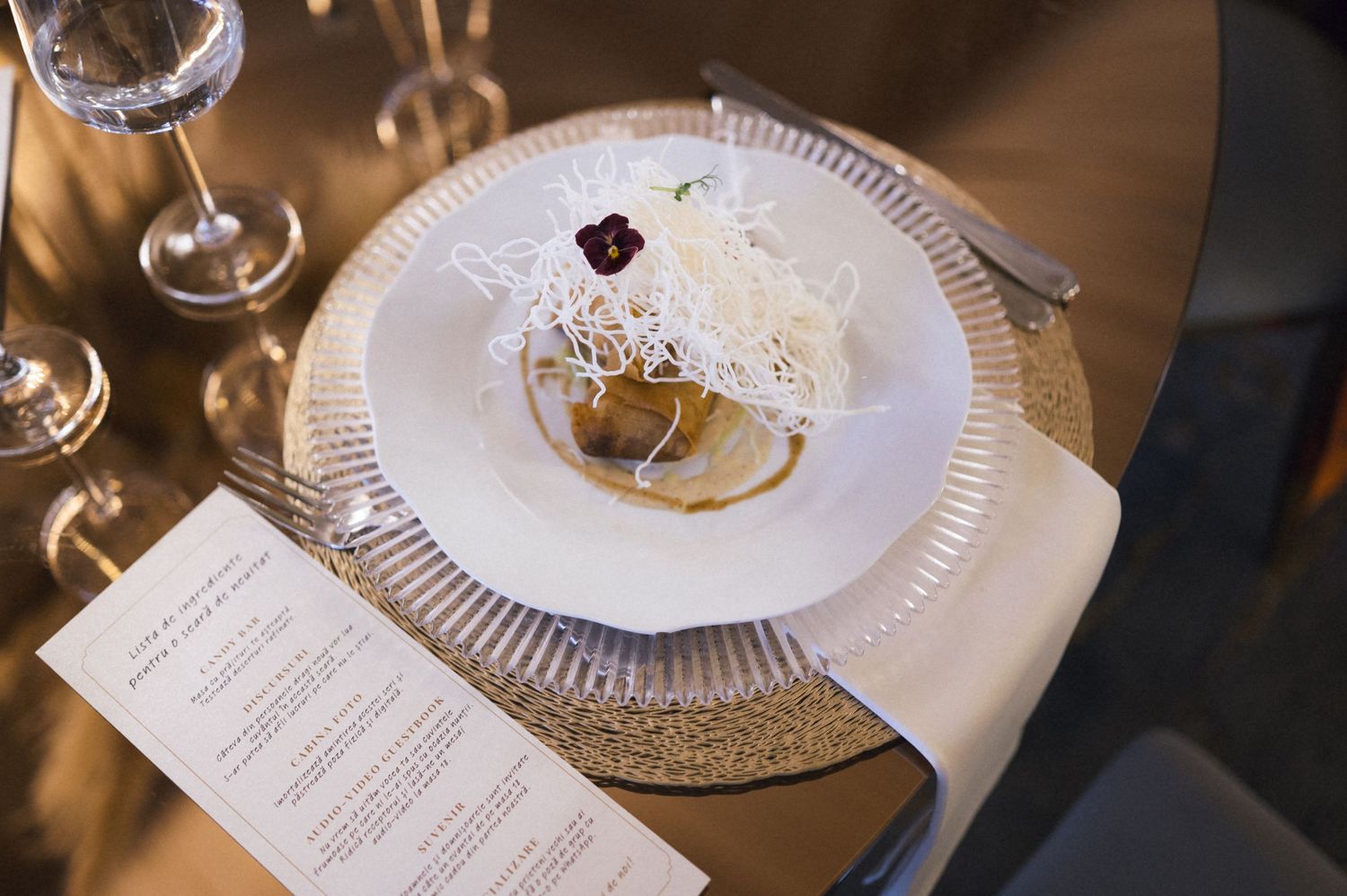 Elegant plated appetizer with shredded garnish on white plate, gold charger, menu card, and crystal glasses at formal dinner.