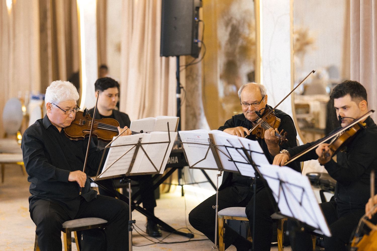 String quartet performing classical music in an elegant hall, four musicians playing violins and viola while reading sheet music.