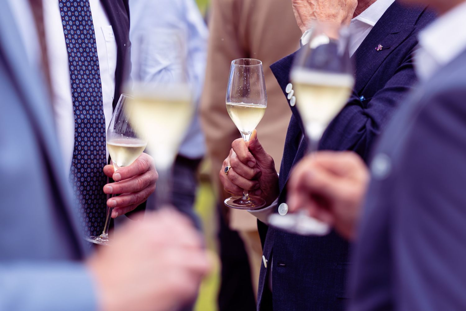 Men in suits holding champagne flutes at a formal celebration or wedding reception.