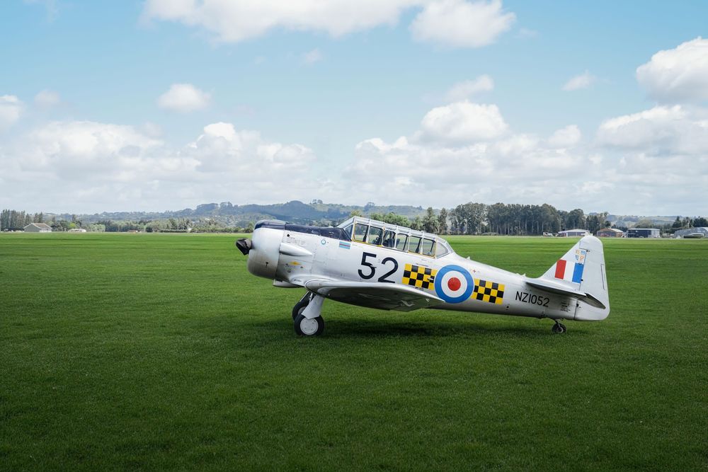 Vintage WWII Harvard trainer aircraft number 52 with RAF roundel markings parked on green airfield under blue sky.