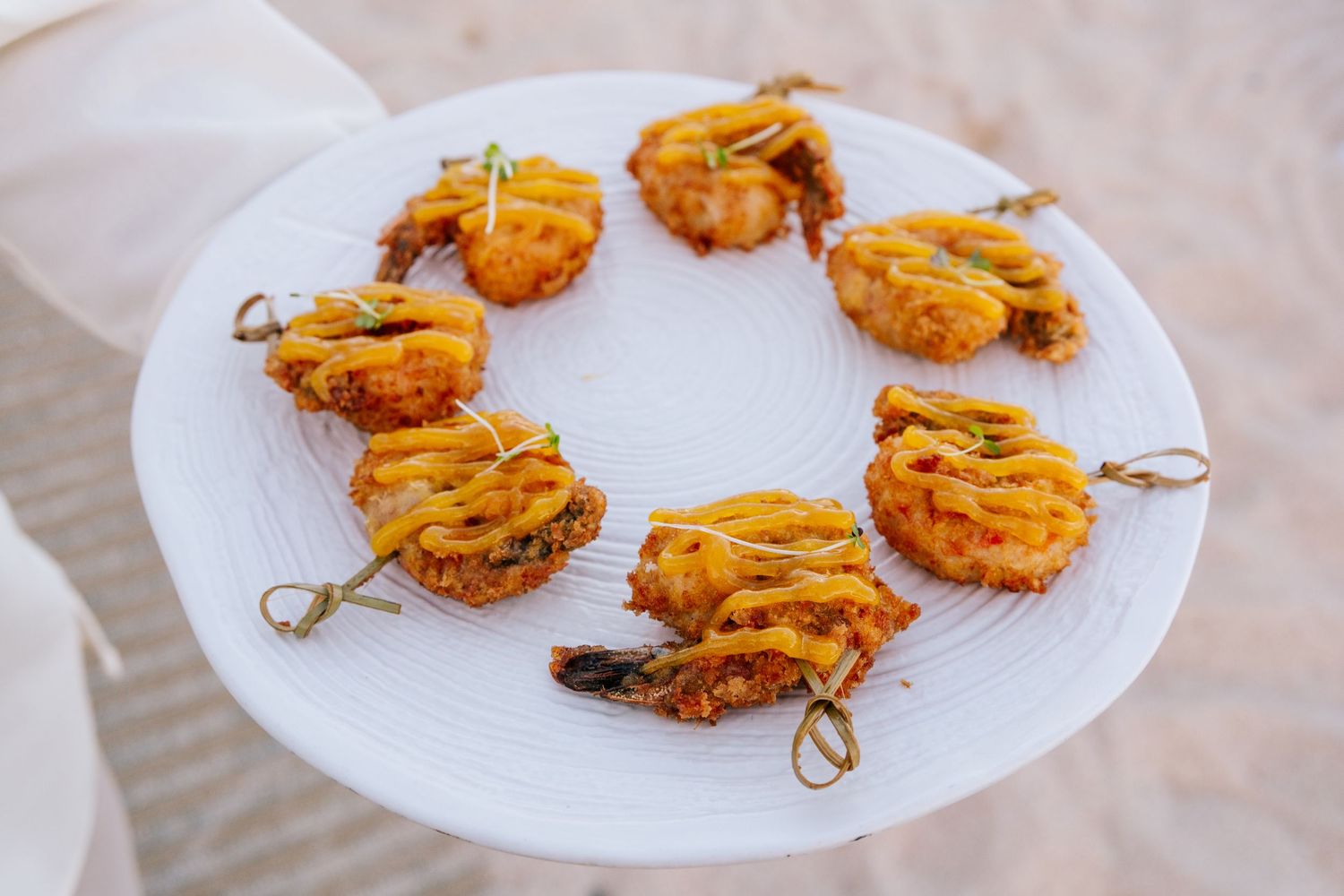 Crispy fried shrimp appetizers arranged in a circle on a white plate, garnished with colorful toppings and skewers.
