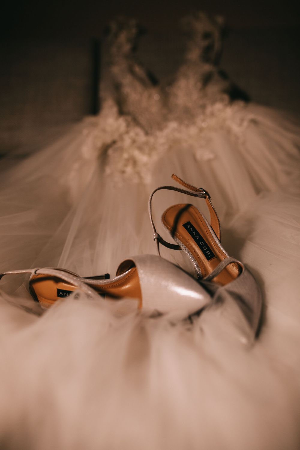Elegant bridal heels resting on a white tulle wedding dress with lace bodice detail.