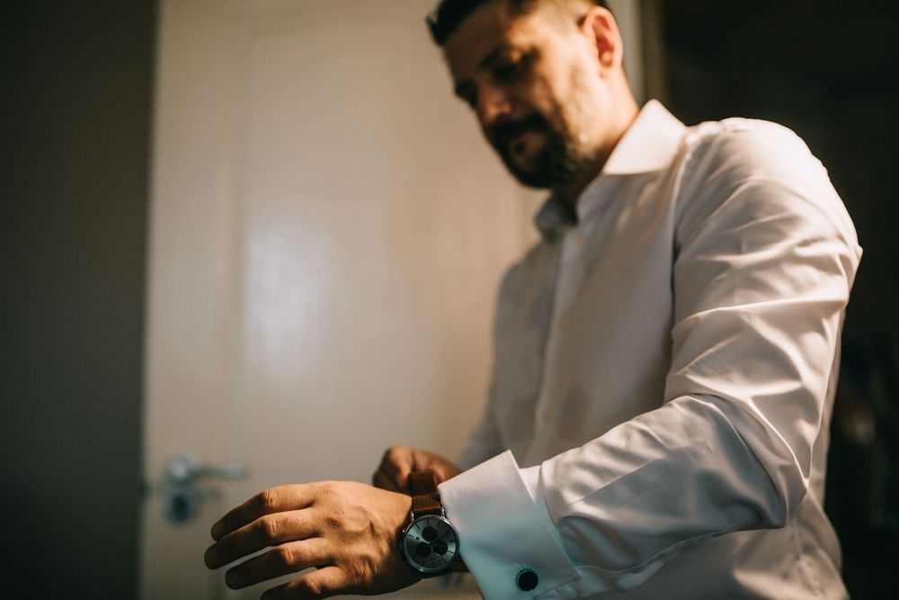Bearded man in white dress shirt checking his wristwatch while getting ready for a formal event.