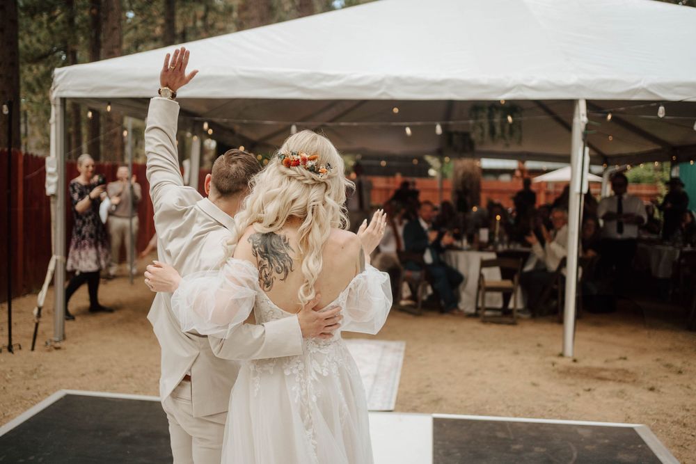 Bride and groom sharing first dance outdoors under white tent with string lights at rustic woodland wedding reception.