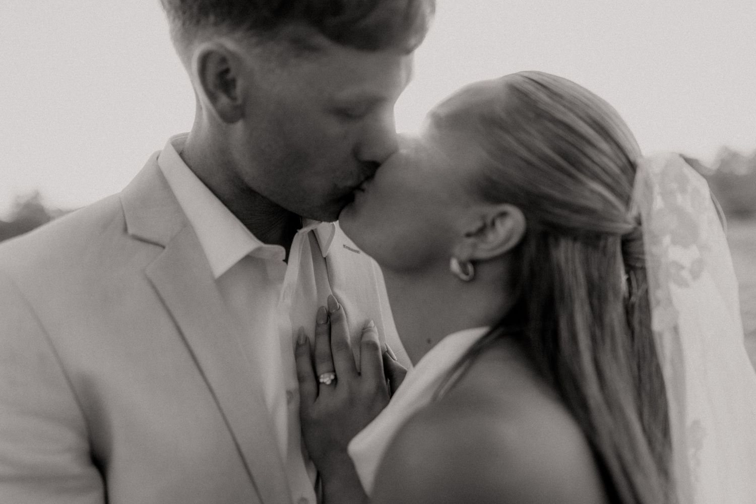 Black and white photo of a bride and groom sharing a kiss on their wedding day, bride wearing veil.