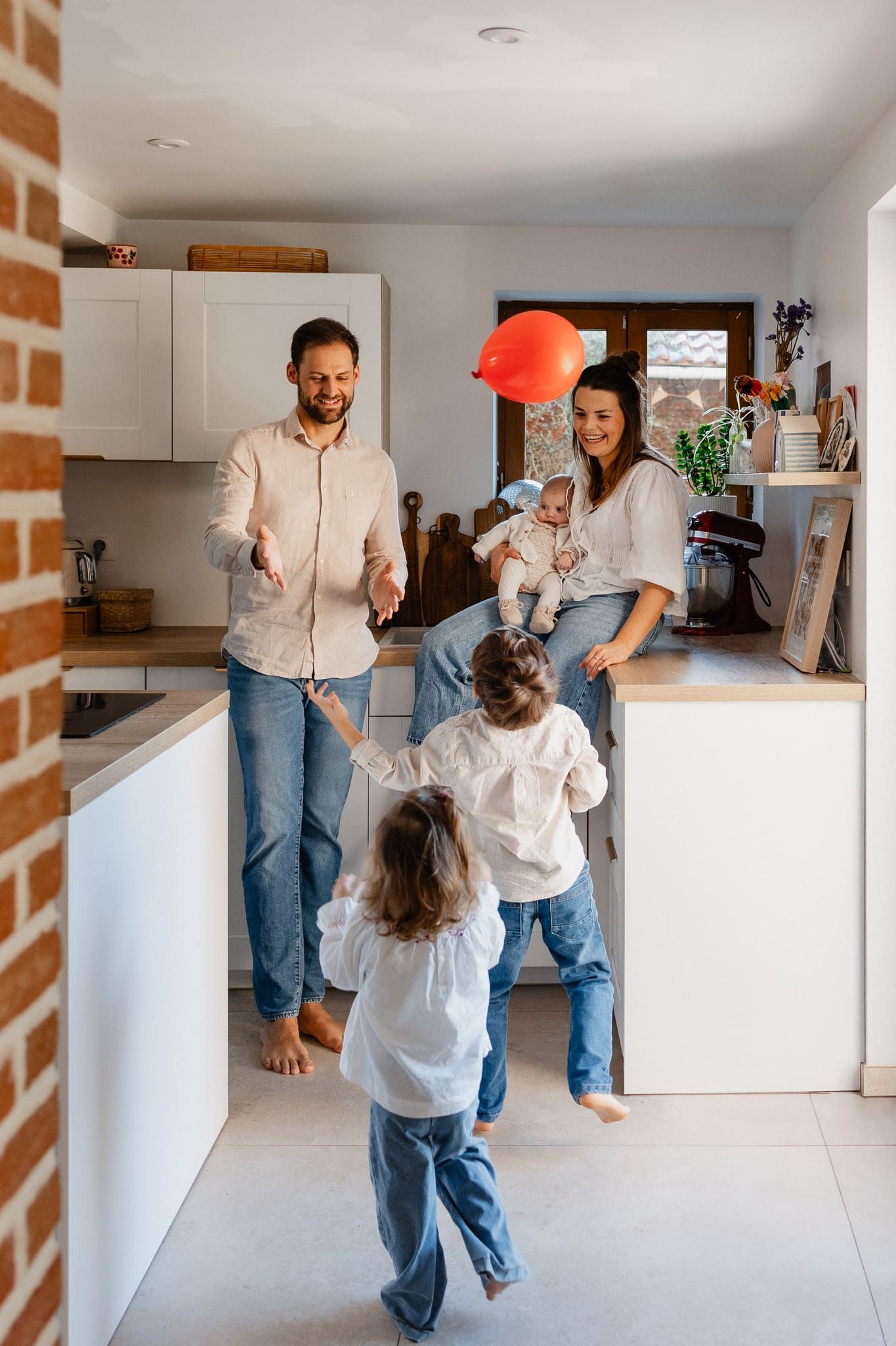 seance photo de famille a domicile a Lambersart pres de Lille, parents et enfants jouent avec un ballon de baudruche dans la cuisine
