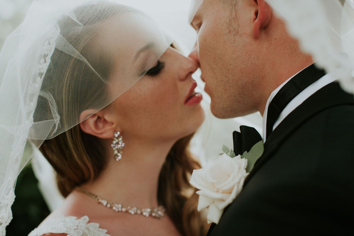 A bride and groom share a romantic kiss under a flowing white veil on their wedding day.