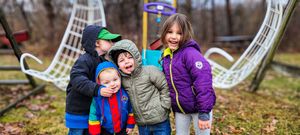 Four young children laughing and hugging together on a playground on a cloudy autumn day.