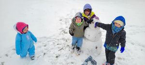 Four children playing in the snow, building a snowman together on a snowy winter day.