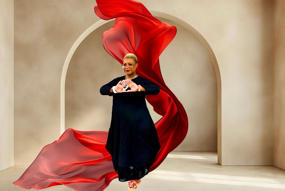 A woman in a black gown poses dramatically with flowing red fabric under an arch.