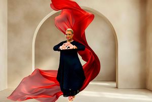 A woman in a black gown poses dramatically with flowing red fabric under an arch.