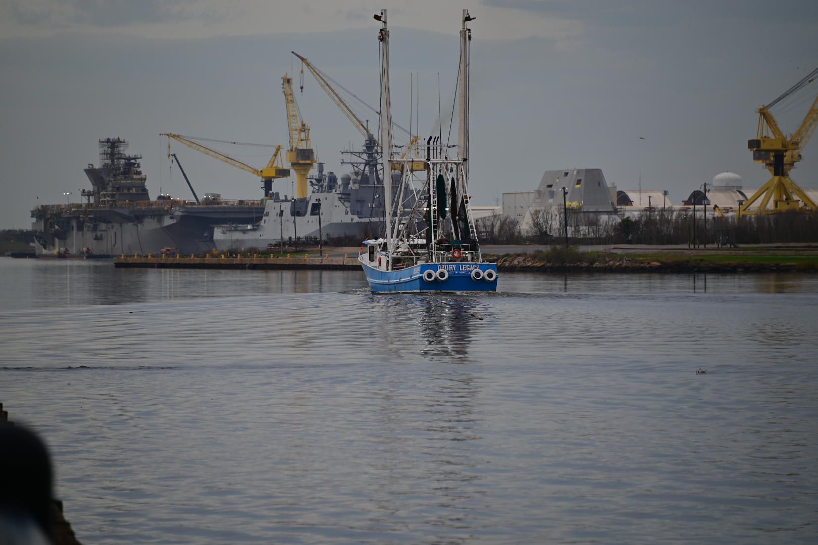 Shrimp boat Drury Legacy heading out past US Navy warships at Ingalls shipyard in Pascagoula, Mississippi