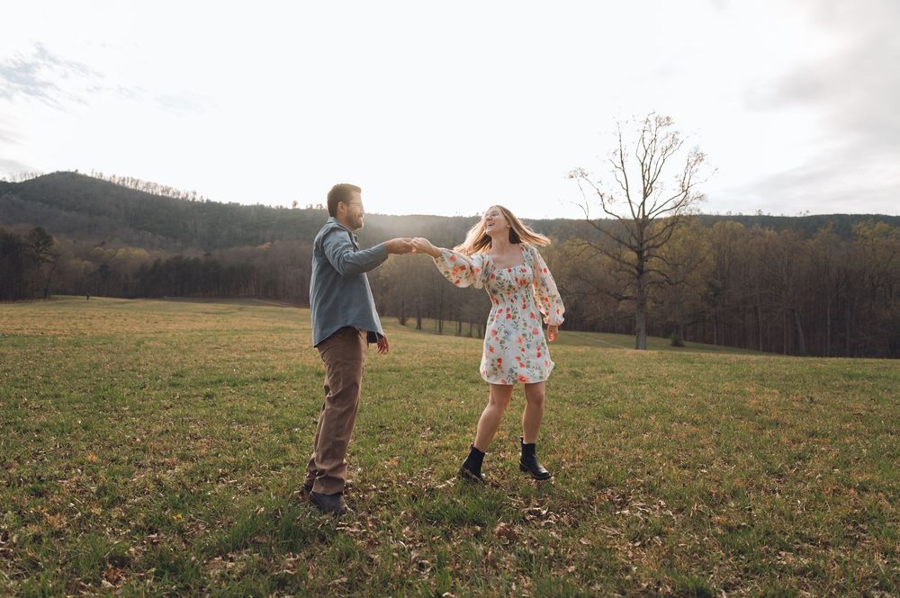 Couple dancing joyfully in a scenic green meadow with rolling hills and trees in the background.