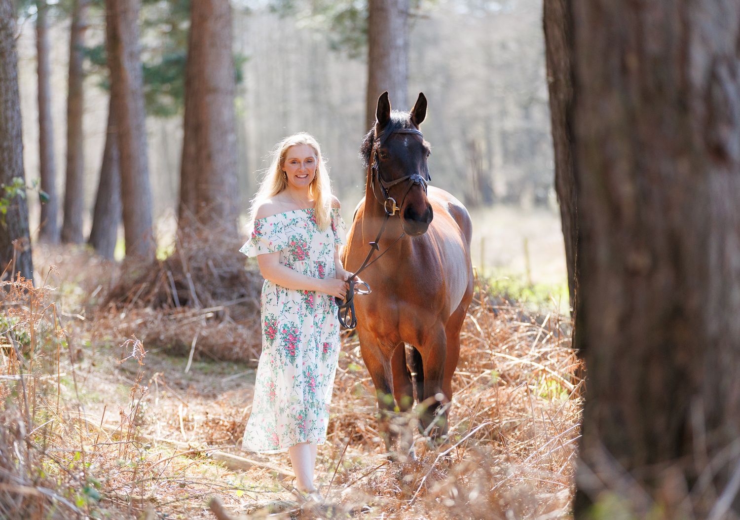 Woman in vintage dress leading a white horse through spring daffodils in a lush green garden.