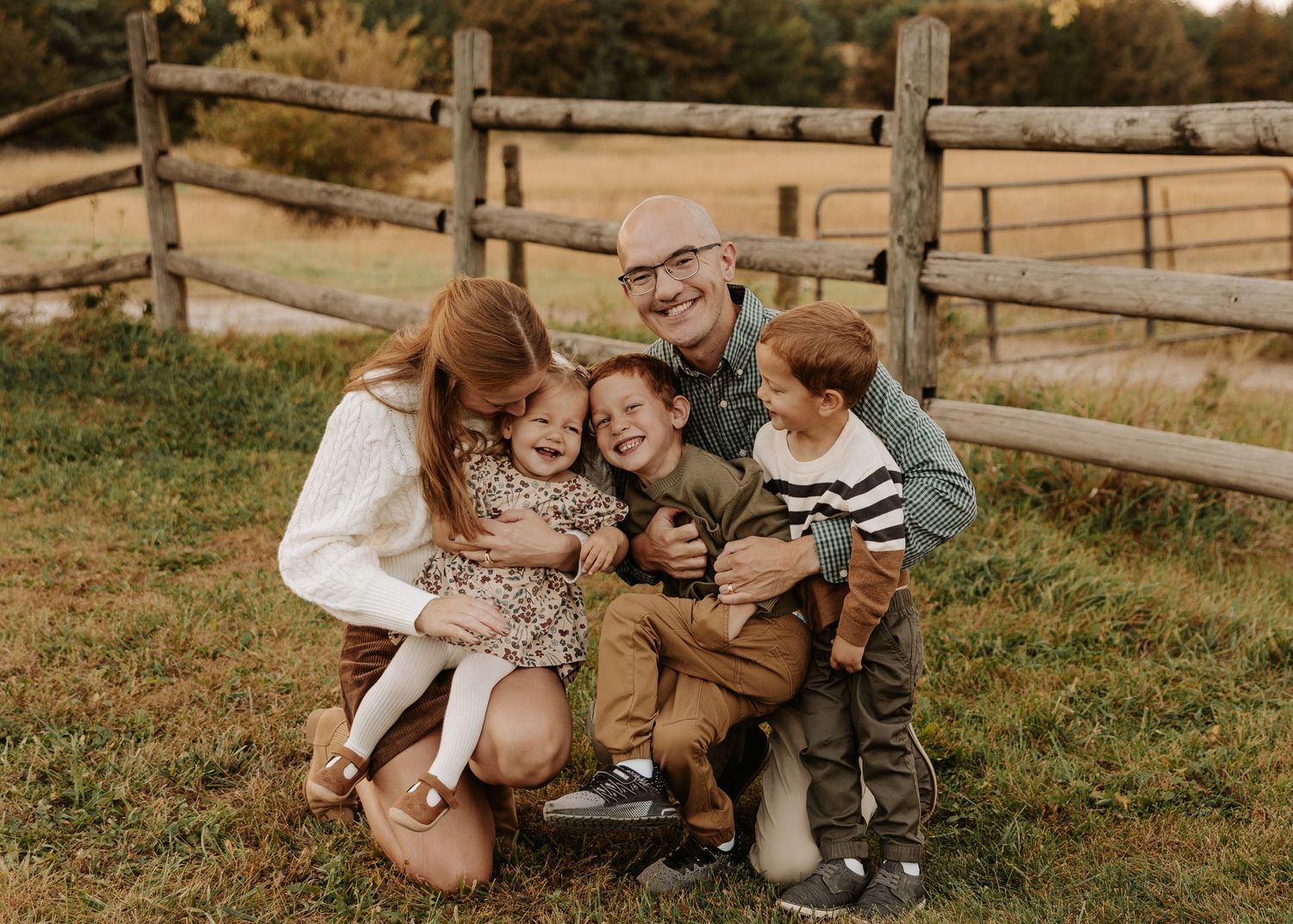 Happy family of five smiling and hugging outdoors near a wooden fence on a green lawn in autumn.