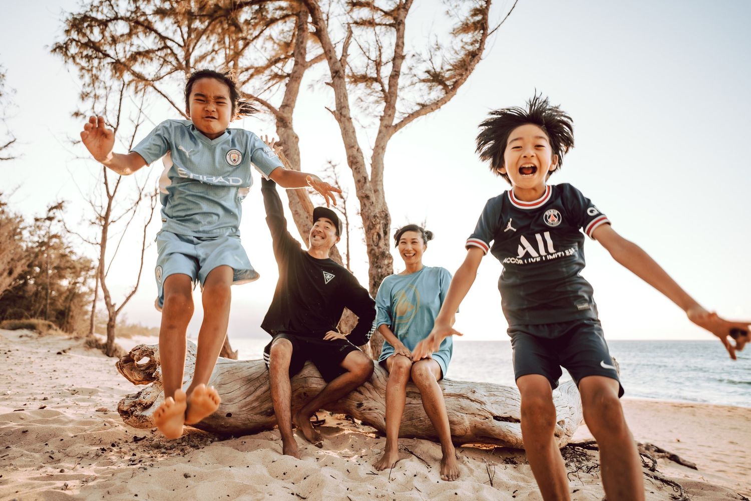 Joyful kids jumping and playing on a sandy beach near a tree at sunset in Maui