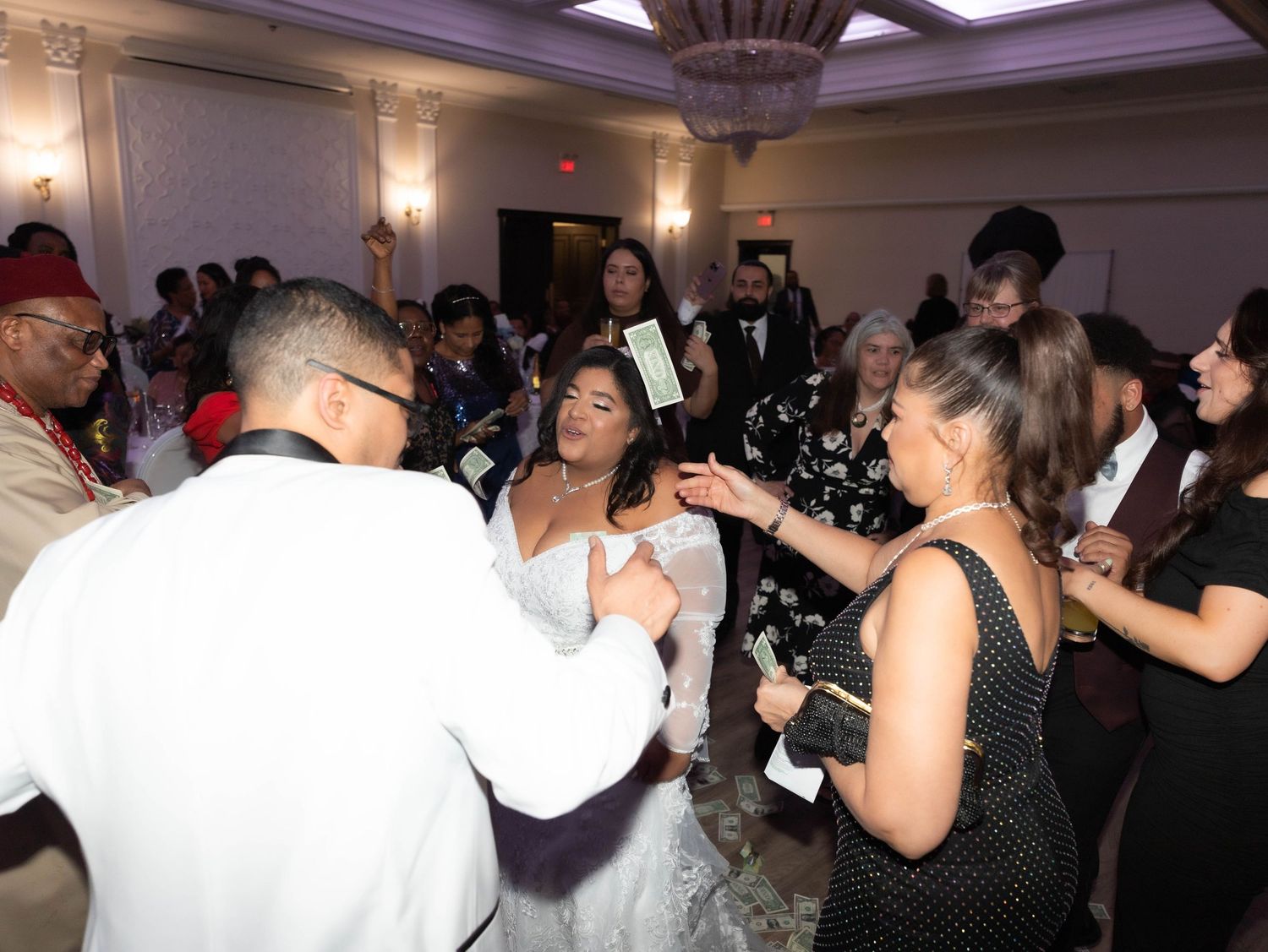 Bride and groom dancing with guests at elegant wedding reception in decorated ballroom.