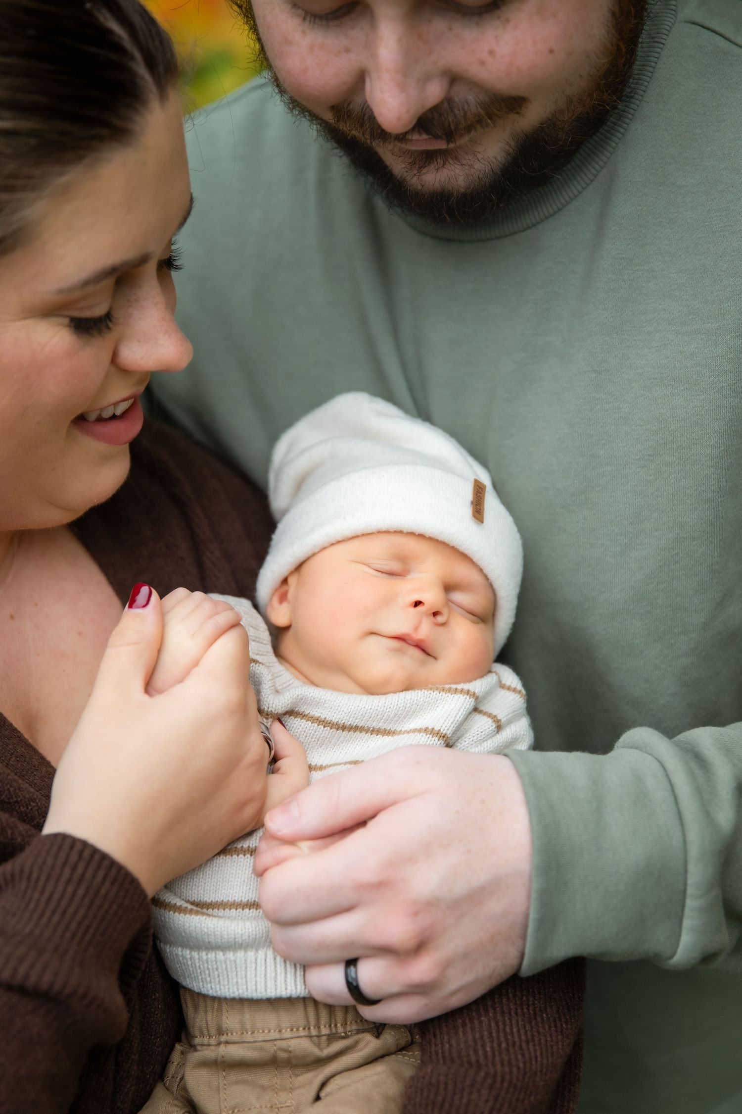 New parents lovingly cradle their sleeping newborn baby dressed in a white hat and striped outfit.