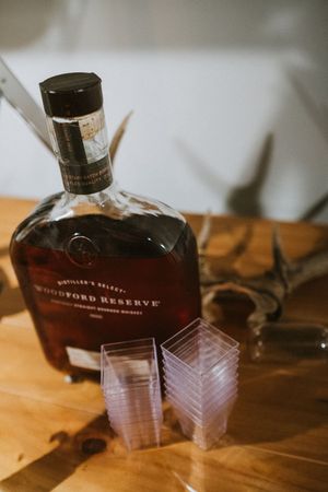 Bottle of Woodford Reserve bourbon whiskey with stacked clear plastic cups and antler decor.