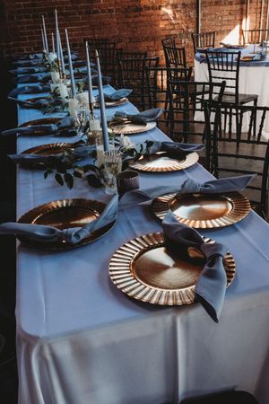 Elegant wedding reception table with gold charger plates, blue napkins, and candlestick centerpieces.