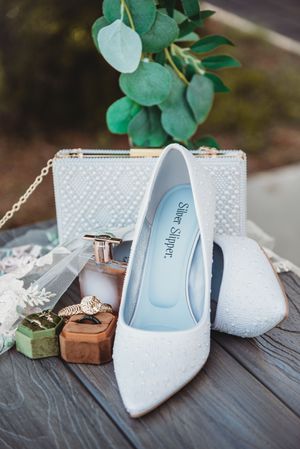 White beaded bridal heels by Silver Slipper with matching clutch, rings, and eucalyptus.