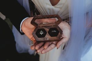 Couple holding a hexagonal wooden ring box with two wedding bands on their wedding day.